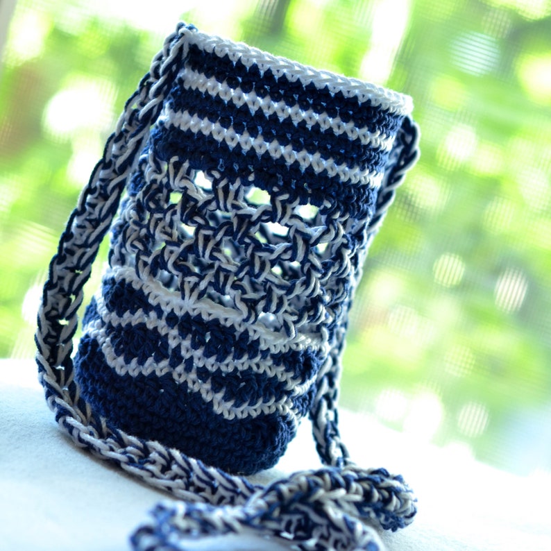 May include: A handmade, blue and white crochet water bottle holder with a long strap. The holder features a striped pattern and an open weave design. The strap is also crocheted in a matching blue and white pattern. The holder is designed to carry a water bottle.