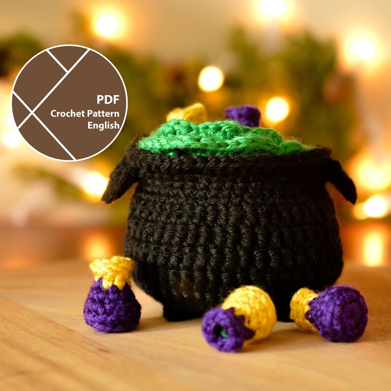 May include: A crocheted black cauldron with green, yellow, and purple accents. The cauldron has two handles and is filled with green crochet. Several small, crocheted pouches in purple and yellow are scattered around the cauldron. The image includes the text "PDF Crochet Pattern English".