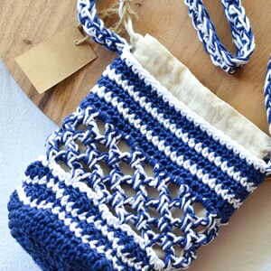 May include: A handmade blue and white crochet bag with a matching strap. The bag has an open weave design and a beige fabric lining. A small tag is attached to the bag.