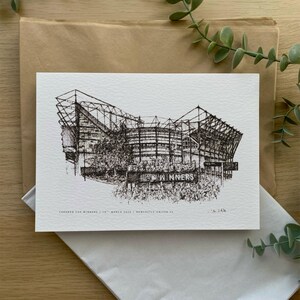 Może przedstawiać: Czarno-biały rysunek pi&oacute;rem i tuszem przedstawiający stadion z napisem "WINNERS" na banerze. Poniżej znajduje się tekst "CARABAO CUP WINNERS, 26TH MARCH 2023 | NEWCASTLE UNITED FC". Rysunek jest na białym papierze.