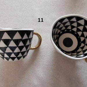 May include: A black and white ceramic coffee mug with a geometric pattern and a gold handle. The inside of the mug has a black and white eye design.