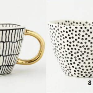 May include: Two white ceramic mugs with gold handles. The mug on the left has a black and white geometric pattern. The mug on the right has a black and white polka dot pattern.