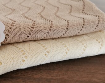 May include: Two knitted blankets, one beige and one white, with a diamond pattern. The blankets are folded and stacked on top of each other.