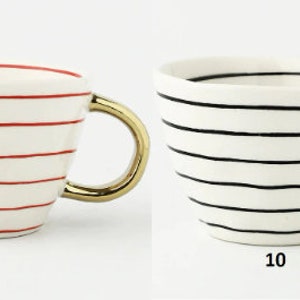 May include: Two ceramic mugs with gold handles. The mug on the left has red stripes and the mug on the right has black stripes. Both mugs are on a white background. 9 and 10 are written below the mugs.