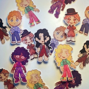 May include: A selection of stickers depicting doll-like characters in various outfits. The stickers feature characters with diverse hairstyles and expressions. The characters are dressed in a range of clothing, including dresses, trousers, and tops, with a mix of colours and patterns.