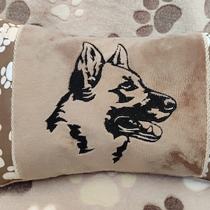 May include: A brown pillow with a white paw print border. The pillow features an embroidered black silhouette of a German Shepherd dog's head.