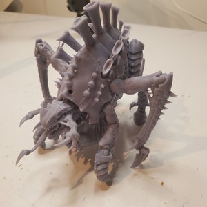 May include: A gray, 3D-printed miniature of a Tyranid creature, featuring a detailed exoskeleton, multiple limbs, and sharp claws. The model has a menacing appearance with a detailed head and multiple dorsal spines, perfect for tabletop gaming or display.