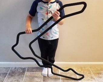 Può includere: Un ritaglio in legno nero di un circuito di corse, tenuto da un bambino. La pista è a forma di otto.