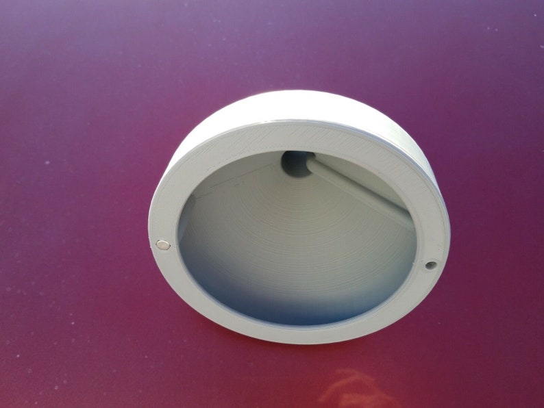 May include: A white plastic round light fitting with a hole in the centre. The fitting is mounted on a red surface.