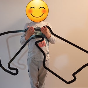 May include: A large, black, curved track, possibly for a toy car race, is held up. The track has a rectangular shape with rounded corners and a winding section. The track is made of a dark material and appears to be a single piece.