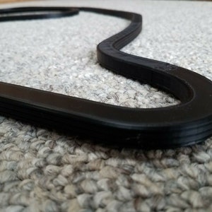 May include: A black rubber race track model in the shape of a figure eight. The track is on a gray carpet.
