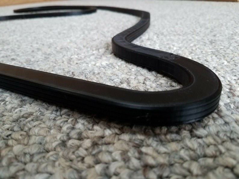 May include: A black rubber race track model in the shape of a figure eight. The track is on a gray carpet.