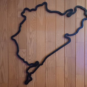 May include: Black outline of a race track on a wood panel wall.