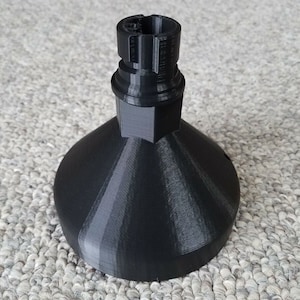 May include: A black 3D-printed object with a conical base and a cylindrical top. The object has a textured surface and appears to be a component or part of a larger assembly. The design is modern and geometric.