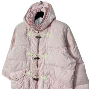 K&ouml;nnte beinhalten: Eine rosafarbene Steppjacke mit Kapuze und Knebelverschl&uuml;ssen. Die Jacke hat ein gestepptes Design und einen Rei&szlig;verschluss.