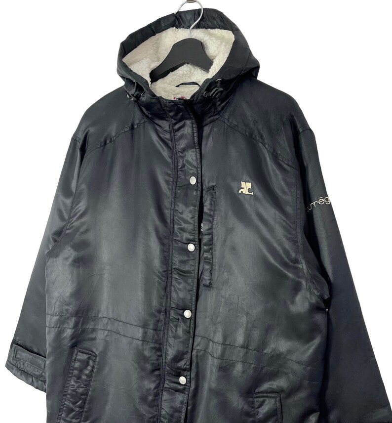 May include: Black hooded jacket with a fleece lining. The jacket has a zipper closure and a button placket. The jacket has a logo on the left chest and the word "omega" on the right sleeve.