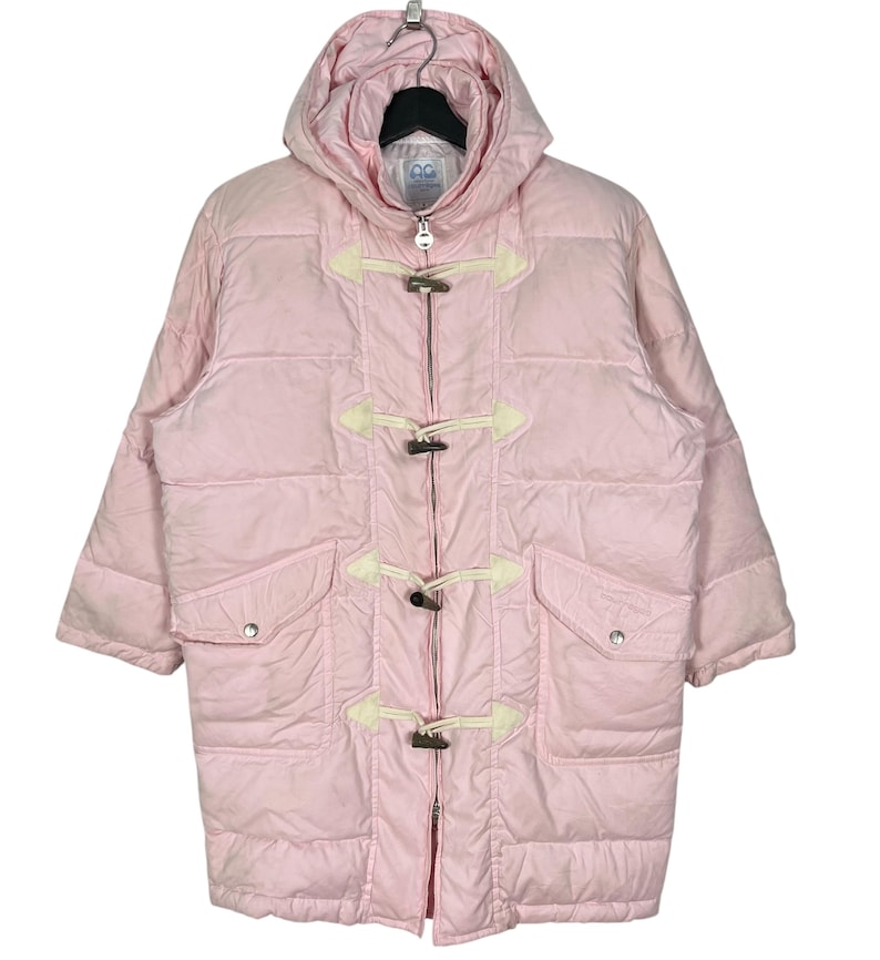 K&ouml;nnte beinhalten: Eine rosafarbene Kapuzen-Steppjacke mit Rei&szlig;verschluss und Knebelverschl&uuml;ssen. Die Jacke hat ein gestepptes Design und zwei Taschen.