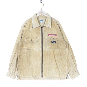 May include: A beige corduroy jacket with a zipper closure and a patch on the left chest that reads "WORLD CHAMPIONSHIP".