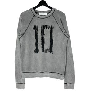 Pode incluir: Camisola cinzenta com o número "10" impresso em preto na frente. A camisola tem gola redonda, mangas compridas e costuras pretas. Está pendurada num cabide preto.