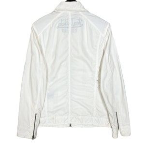 K&ouml;nnte beinhalten: Wei&szlig;e Rei&szlig;verschlussjacke mit einem Von Dutch Logo auf der R&uuml;ckseite. Die Jacke hat einen Kragen und lange &Auml;rmel.