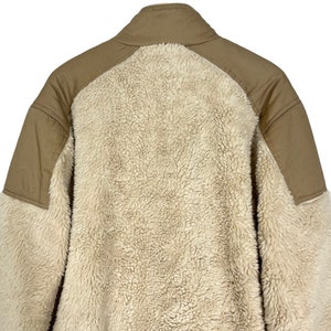 May include: A beige fleece jacket with brown canvas panels on the shoulders and back. The jacket has a high collar and a zipper closure.