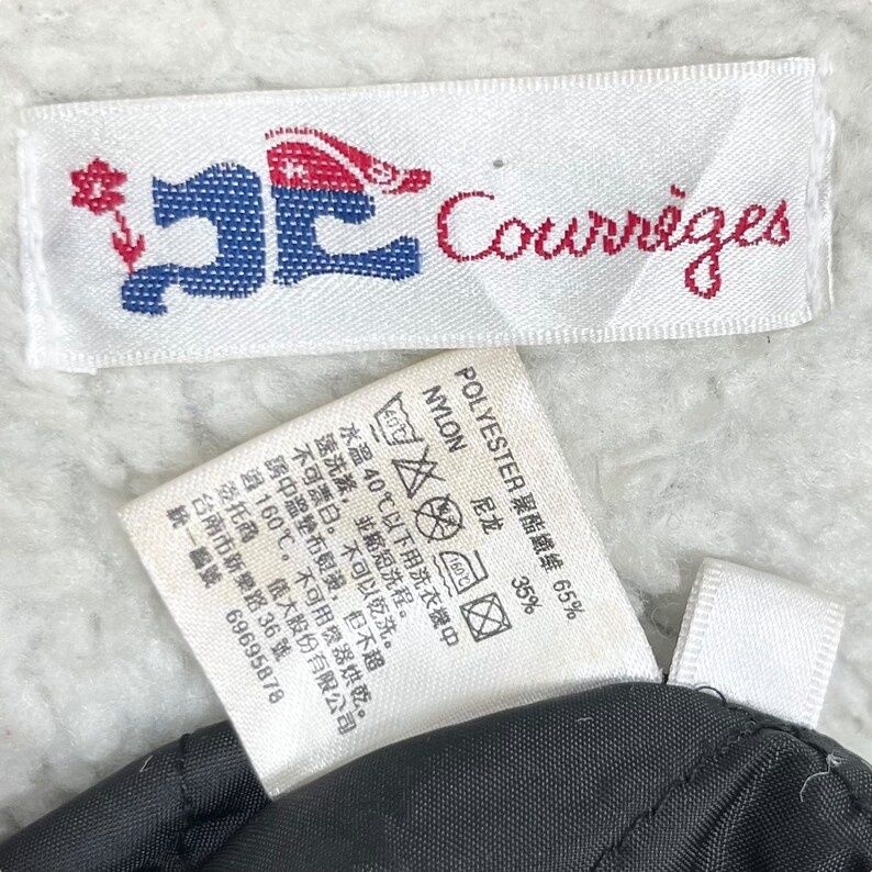 May include: White label with a red, white, and blue logo that says "Courr&egrave;ges" in red. A second white label with black text shows the fabric composition: 65% polyester and 35% nylon. The label also includes care instructions in Japanese.