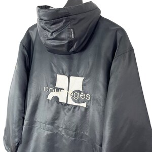 May include: Black hooded jacket with a white "Courreges" logo on the back. The jacket has a zipper closure and a drawstring hood.