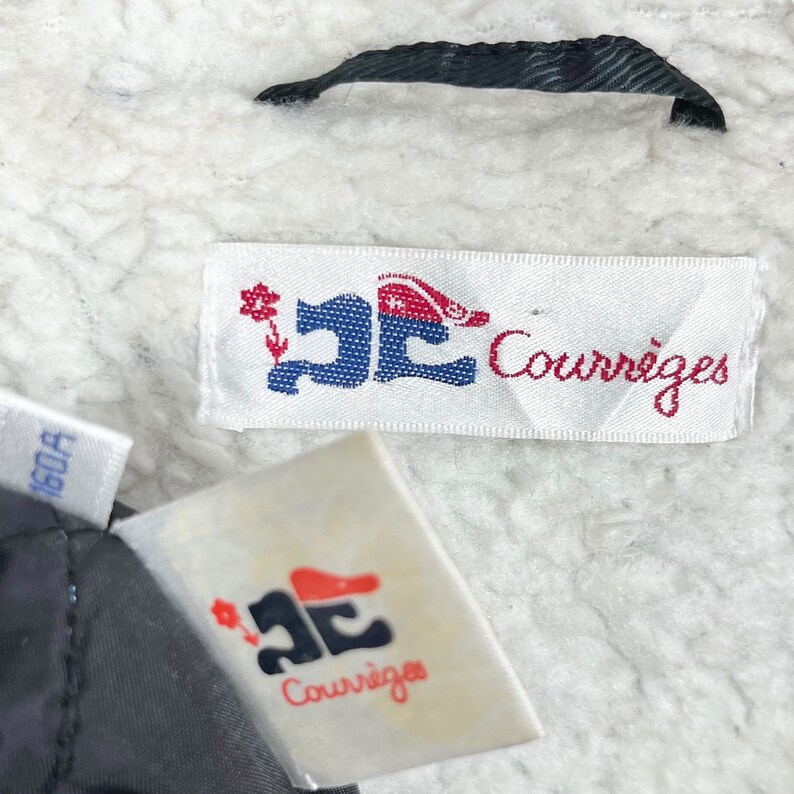 May include: Two white fabric labels with the text "Courr&egrave;ges" in black and a stylized logo in blue, red, and white. The logo features a flower, a shoe, and a hat.