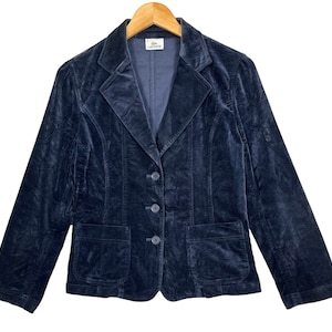 May include: A dark blue velvet blazer with a single button closure and two front pockets. The blazer has a "LACOSTE" label on the inside.