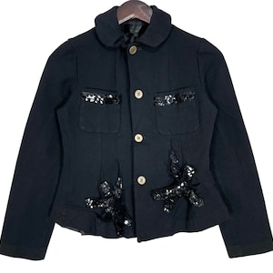 May include: A black blazer with a peter pan collar and gold buttons. The blazer has sequin embellishments on the pockets and the bottom hem.