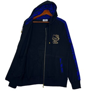 May include: Black zip-up hoodie with a blue and black zebra print on the sleeves and hood. The hoodie features a gold Hello Kitty graphic on the front.