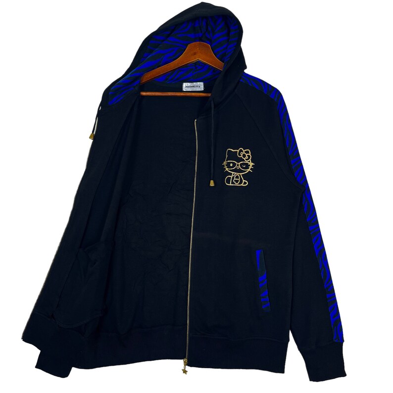 May include: Black zip-up hoodie with a blue and black zebra print on the sleeves and hood. The hoodie features a gold Hello Kitty graphic on the front.