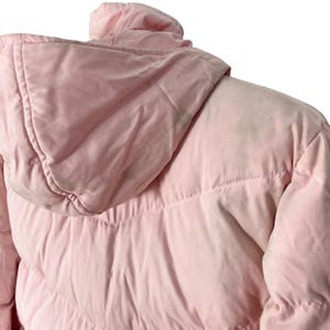 K&ouml;nnte beinhalten: Eine rosafarbene Steppjacke mit Kapuze. Die Jacke hat ein gestepptes Design und ist aus einem weichen, leichten Stoff gefertigt.