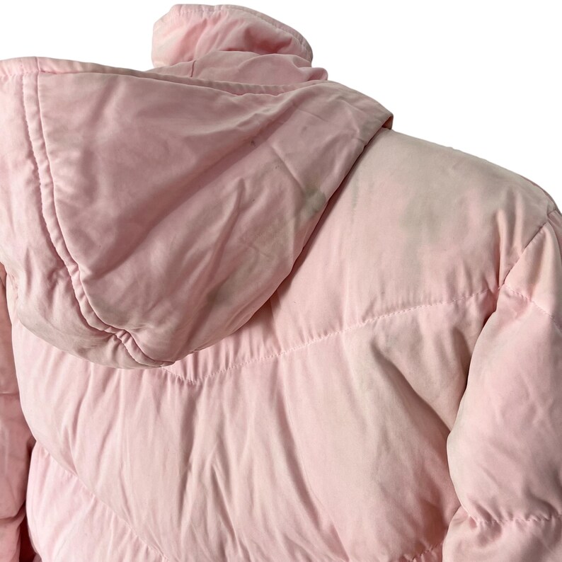 K&ouml;nnte beinhalten: Eine rosafarbene Steppjacke mit Kapuze. Die Jacke hat ein gestepptes Design und ist aus einem weichen, leichten Stoff gefertigt.