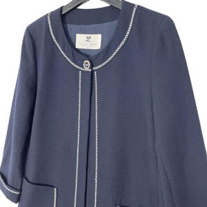 May include: A navy blue blazer with a white chain trim around the neckline and down the front. The blazer has a single button closure and a small pocket on the left side. The label "JC Courr&egrave;ges" is visible on the inside of the blazer.