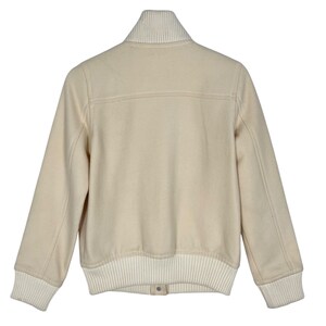 May include: Cream-colored bomber jacket with a ribbed collar, cuffs, and hem. The jacket features a button closure and a classic design. The sleeves are long, and the jacket is made of a soft, textured material.