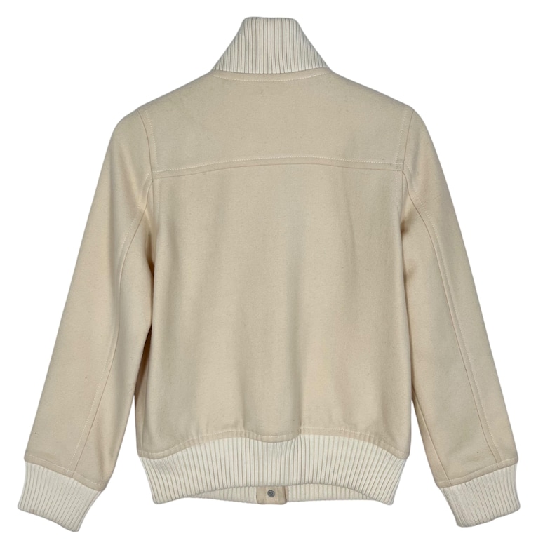 May include: Cream-colored bomber jacket with a ribbed collar, cuffs, and hem. The jacket features a button closure and a classic design. The sleeves are long, and the jacket is made of a soft, textured material.