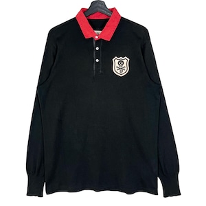 Op de afbeelding: Zwart langarm rugby shirt met een rode kraag en een schedel en gekruiste botten patch op de borst.