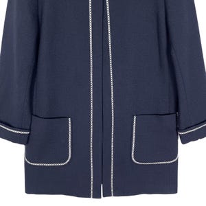 May include: A navy blue jacket with white trim around the edges and pockets. The jacket has a long, fitted silhouette.