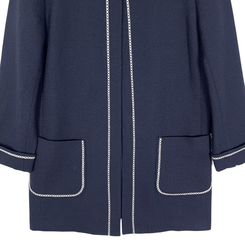 May include: A navy blue jacket with white trim around the edges and pockets. The jacket has a long, fitted silhouette.