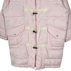 K&ouml;nnte beinhalten: Eine rosafarbene Steppjacke mit Rei&szlig;verschluss und Knebelverschl&uuml;ssen. Die Jacke hat zwei Taschen und ein wei&szlig;es Logo auf der rechten Tasche.