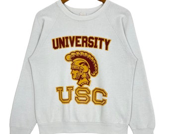 May include: White sweatshirt with a red and gold University of Southern California (USC) logo. The logo features a Trojan warrior's helmet and the words "UNIVERSITY" and "USC".