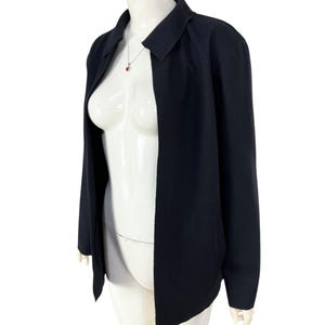 May include: A black blazer with a collar and two front pockets. The blazer is open in the front and is displayed on a mannequin. A silver necklace with a red pendant is visible.