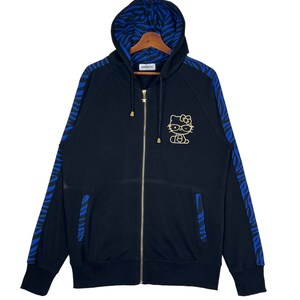 May include: Black zip-up hoodie with blue and black zebra print on the sleeves and hood. The hoodie has a gold Hello Kitty graphic on the front.