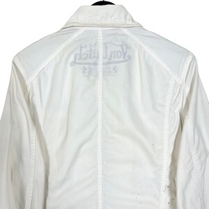 K&ouml;nnte beinhalten: Wei&szlig;e Jacke mit einem gro&szlig;en "Von Dutch" Logo auf der R&uuml;ckseite. Das Logo ist in einer stilisierten Schriftart gehalten und enth&auml;lt die W&ouml;rter "Los Angeles" und "California".