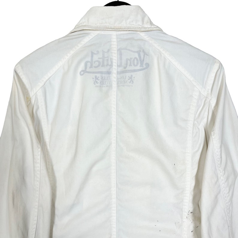 K&ouml;nnte beinhalten: Wei&szlig;e Jacke mit einem gro&szlig;en "Von Dutch" Logo auf der R&uuml;ckseite. Das Logo ist in einer stilisierten Schriftart gehalten und enth&auml;lt die W&ouml;rter "Los Angeles" und "California".
