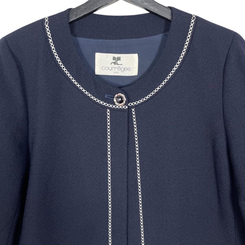 May include: A navy blue blazer with white stitching around the collar and down the front. The blazer has a single button closure and a label that reads "Courr&egrave;ges Paris".