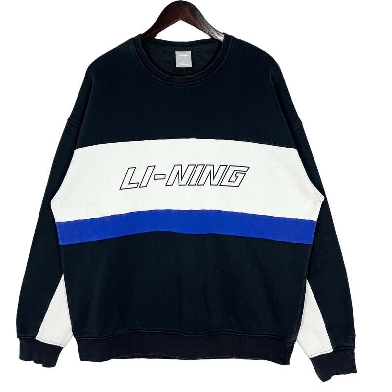 May include: Black sweatshirt with white and blue horizontal stripes. The sweatshirt has the text "LI-NING" in white outlined in black on the white stripe.