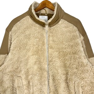 May include: A beige sherpa jacket with brown corduroy accents on the shoulders and sleeves. The jacket has a zipper closure and a stand-up collar.