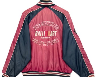 Op de afbeelding: Een rood en zwart baseballjack met de tekst "The Spirit of Ralliart Club Man Competition" op de achterkant.